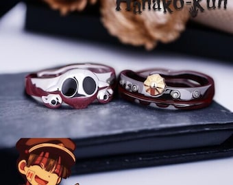 May include: Two silver rings with red and black accents. One ring features a skull design with large black eyes, while the other has a gold-colored center and circular details. The rings are displayed on a dark surface with the text "Toilet-bound Hanako-Kun".