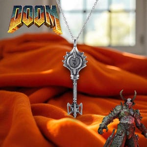 May include: Silver key pendant necklace with a detailed design. The key features a circular emblem and a decorative handle. The word "DOOM" is displayed in a 3D style in the upper left corner. The background is a textured orange fabric.