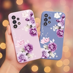 May include: Two phone cases, one lavender and one blue, are adorned with floral designs. The lavender case features a cluster of purple and white flowers, while the blue case has a similar arrangement. Both cases have camera cutouts.