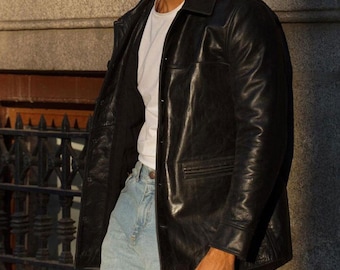 May include: A black leather jacket with a collared neckline and button closure. The jacket is worn over a white t-shirt and light blue jeans. The jacket has a classic, tailored design.