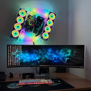 Puede incluir: Configuración de PC para juegos con un monitor curvo, un teclado retroiluminado y un ratón. La carcasa del PC está montada en la pared con ventiladores LED. El escritorio también tiene una alfombrilla de ratón y auriculares.