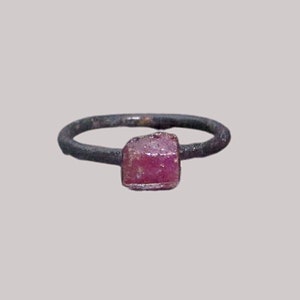 May include: A simple silver ring with a square, faceted, pink gemstone.