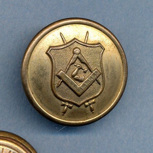 May include: Two antique brass buttons. One button features a Masonic emblem within a shield, with tools and symbols. The other button is stamped with the text "ACME HALL BALTIMORE OEHM'S".