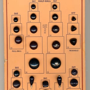 May include: A vintage display card of black shoe buttons in various shapes, including half-ball, full-ball, and triangle. The card has text reading "Shoe Buttons!!" and "All Colors Dyed to Match!!!" with sizes in mm.