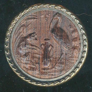 May include: A round, brown button with a detailed relief of two birds and foliage. The button has a gold-colored, rope-like border and a silver-colored inner ring. The birds are intricately carved, showcasing the button's craftsmanship.
