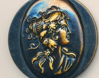May include: An oval-shaped, dark blue ceramic button with a relief of a woman's profile. The woman's hair is adorned with grapes and leaves, and the relief is in shades of gold and yellow. The button has a metallic sheen.