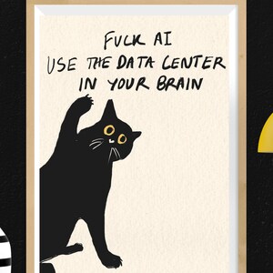 May include: A framed wall art print featuring a black cat illustration on a cream background. The cat has yellow eyes and one raised paw. The text reads: FUCK AI USE THE DATA CENTER IN YOUR BRAIN. The frame is light wood, and the print is rectangular.