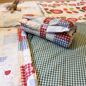 May include: Several patchwork quilts and blankets are displayed, showcasing diverse patterns and colours. One quilt features elephant and heart motifs. Another has a red and white floral design. A wrapped item is secured with red and white gingham ribbon. A toy airplane is also visible.