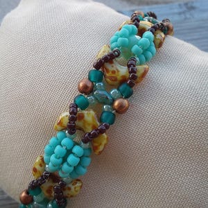 May include: A beaded bracelet featuring a repeating pattern of turquoise blue seed bead clusters, brown seed beads, metallic copper-toned beads, and crescent-shaped beads with a yellow and brown mottled pattern arranged in a woven design.