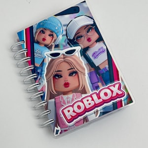 Può includere: Un taccuino a spirale con una stampa grafica di tre personaggi stilizzati dai tratti squadrati. La copertina mostra il testo ROBLOX in un carattere rosso e bianco in grassetto, insieme a personaggi che indossano cappelli, occhiali e abbigliamento casual nei toni del blu, bianco e rosa.