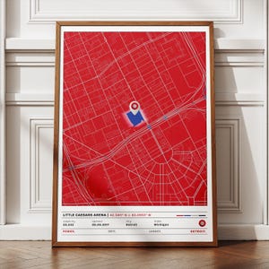 Op de afbeelding: Een ingelijste print met een rood-witte kaart van Detroit, Michigan, met een blauwe markering. De print bevat tekst met details over Little Caesars Arena, inclusief de capaciteit en openingsdatum.