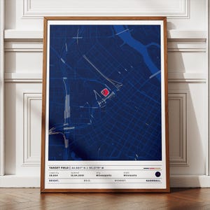 May include: A framed print featuring a detailed blue and white map of a city, with a red stadium highlighted. The text at the bottom reads "TARGET FIELD" and includes details about the stadium's capacity, opening date, and location. The word "BASEBALL" is also visible.
