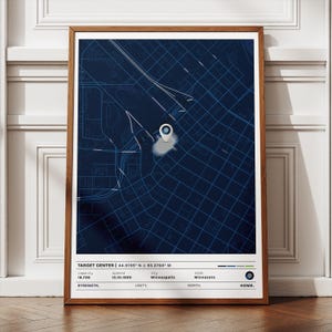May include: A framed print featuring a detailed map of an urban area, with a highlighted location marked by a pin. The map is rendered in shades of blue, with white lines indicating roads and infrastructure. Text at the bottom reads "TARGET CENTER" and includes coordinates, capacity, and opening date.