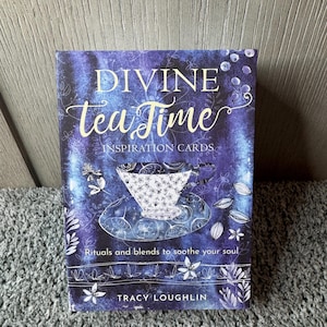 Puede incluir: Una baraja de "Divine Tea Time Inspiration Cards" con un fondo azul y morado. La portada presenta un dise&ntilde;o de taza de t&eacute; y el texto "Rituals and blends to soothe your soul" y el nombre del autor, Tracy Loughlin.
