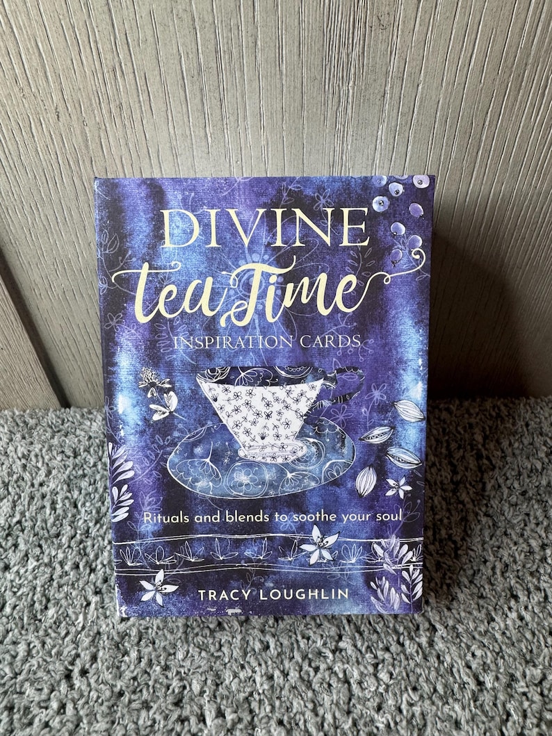 Puede incluir: Una baraja de "Divine Tea Time Inspiration Cards" con un fondo azul y morado. La portada presenta un dise&ntilde;o de taza de t&eacute; y el texto "Rituals and blends to soothe your soul" y el nombre del autor, Tracy Loughlin.