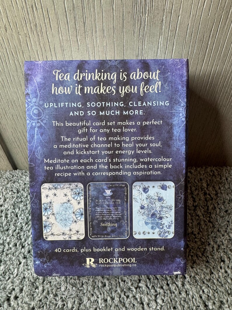 Puede incluir: Un juego de cartas con tem&aacute;tica de t&eacute; en tonos morados y azules, con el texto "Tea drinking is about how it makes you feel!" y "Uplifting, Soothing, Cleansing and so much more." El set incluye 40 cartas, un folleto y un soporte de madera.