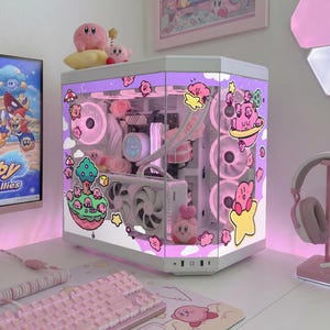 May include: A custom-built computer case with a pink and white theme, featuring Kirby character decals. The case is illuminated with pink lights and has a clear side panel. A matching pink keyboard, mousepad, and headset complete the setup.