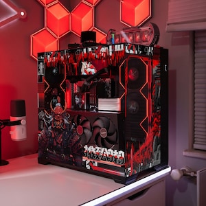 May include: A custom PC tower with a red and black aesthetic. The design incorporates a Japanese warrior illustration and Japanese text. Internal components are visible, lit by red lights. The computer is on a white desk, with a red wall in the background.
