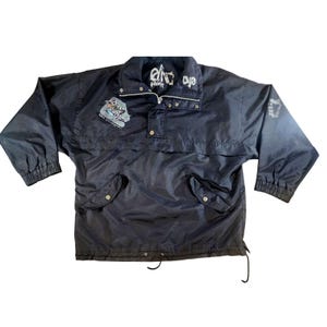 May include: A navy blue anorak jacket with a high collar and a half-zip closure. The jacket features a small embroidered patch on the chest and the text "eye freestyle" on the collar. The sleeves have elastic cuffs, and the jacket has two front pockets.