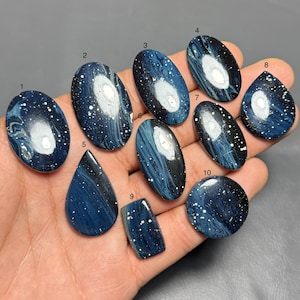 May include: Ten polished cabochons numbered one through ten, featuring a dark blue and black marbled pattern with white speckles resembling a night sky. The stones vary in oval, teardrop, rectangular, and circular shapes with smooth surfaces.