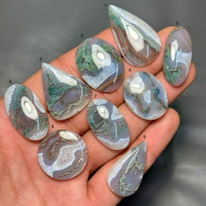 Può includere: Nove pietre preziose cabochon lucidate numerate da uno a nove, caratterizzate da motivi in agata traslucida color lavanda e bianco con complesse inclusioni verdi simili a muschio. Ogni pietra presenta una superficie liscia e arrotondata.