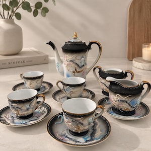Peut inclure: Un service à thé en porcelaine comprenant une théière, un pot à lait, un sucrier et quatre tasses avec soucoupes assorties. Chaque pièce présente un dégradé noir, des bords dorés et des motifs de dragon en relief aux tons blanc et bleu.