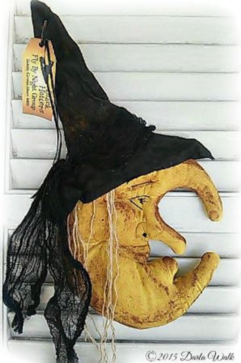 Puede incluir: Una luna creciente amarilla con cara de bruja y un sombrero de bruja negro. El sombrero tiene una etiqueta que dice "Witch Hat Fly By Night Creations".