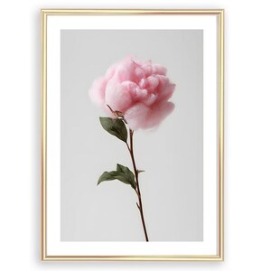 Pode incluir: Uma impressão artística emoldurada com uma única flor rosa com uma aparência fofa, semelhante a uma nuvem. A flor está em uma haste marrom com folhas verdes, em um fundo macio e claro. A moldura é dourada.