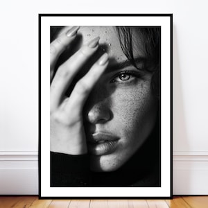 Puede incluir: Retrato enmarcado en blanco y negro de una persona con pecas, parcialmente cubierta por una mano. El ojo es visible, con gotas de agua en la frente. La imagen es un primer plano, que enfatiza los detalles faciales.
