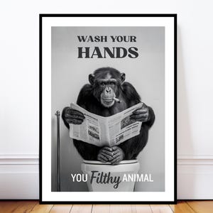 May include: Black and white framed print featuring a chimpanzee sitting on a toilet, smoking a cigarette, and reading a newspaper. The text "WASH YOUR HANDS" and "YOU Filthy ANIMAL" are displayed.