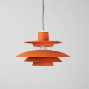 Op de afbeelding: Oranje hanglamp met een gelaagd ontwerp. De lamp hangt aan een zwart snoer en heeft een cilindrische bovenkant. De gloeilamp is zichtbaar in het midden van de lamp.