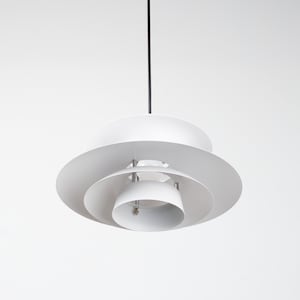 Op de afbeelding: Een witte, gelaagde hanglamp met een cirkelvormig ontwerp. De lamp heeft meerdere niveaus van gebogen, schijfvormige kappen, opgehangen aan een zwart snoer. De armatuur is een modern, minimalistisch ontwerp.