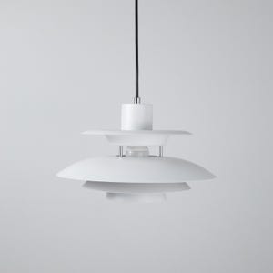 Op de afbeelding: Een witte, moderne hanglamp met een meerlaags kapontwerp. De lamp heeft een cirkelvormige bovenkant, een middelste laag en een onderste laag, allemaal in het wit. De lamp hangt aan een zwart snoer en is geschikt voor binnenverlichting.