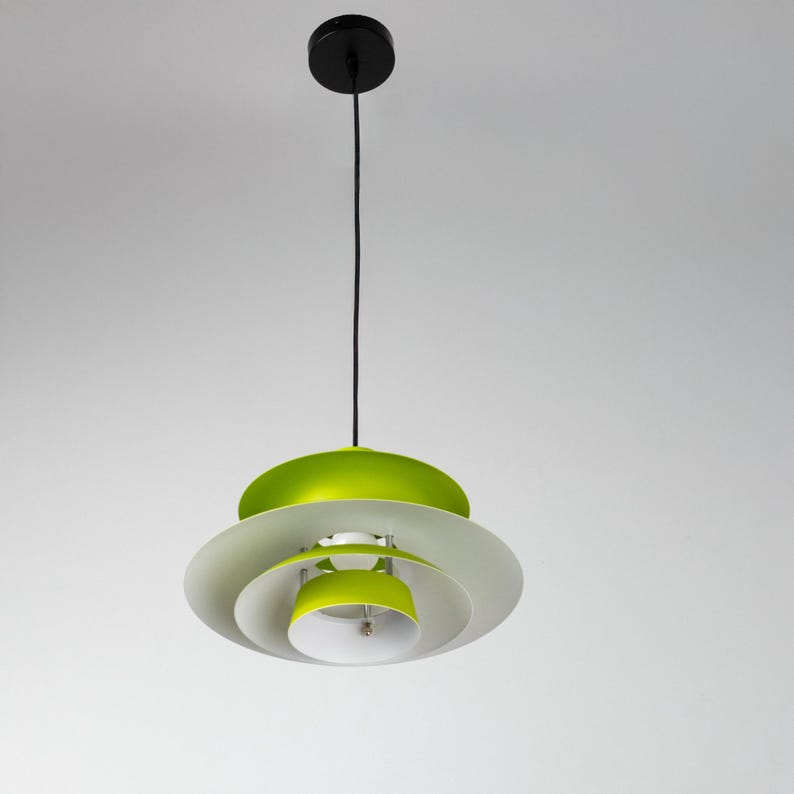 Op de afbeelding: Een moderne hanglamp met een gelaagd ontwerp. De lamp heeft een zwarte plafondbevestiging, een zwart snoer en overlappende, cirkelvormige kappen in wit, groen en wit. De lamp hangt tegen een effen witte achtergrond.