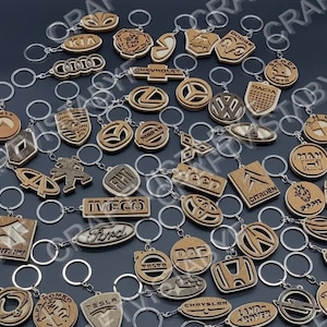May include: A collection of wooden keychains featuring various car brand logos, including Kia, Audi, Chevrolet, and others. Each keychain has a silver ring and is made of light brown wood. The logos are intricately carved.