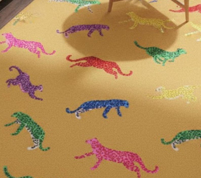 May include: A mustard-colored rug featuring a repeating pattern of colorful cheetahs. The cheetahs are depicted in various colors, including pink, purple, blue, green, and yellow. The rug is likely made of a soft material.