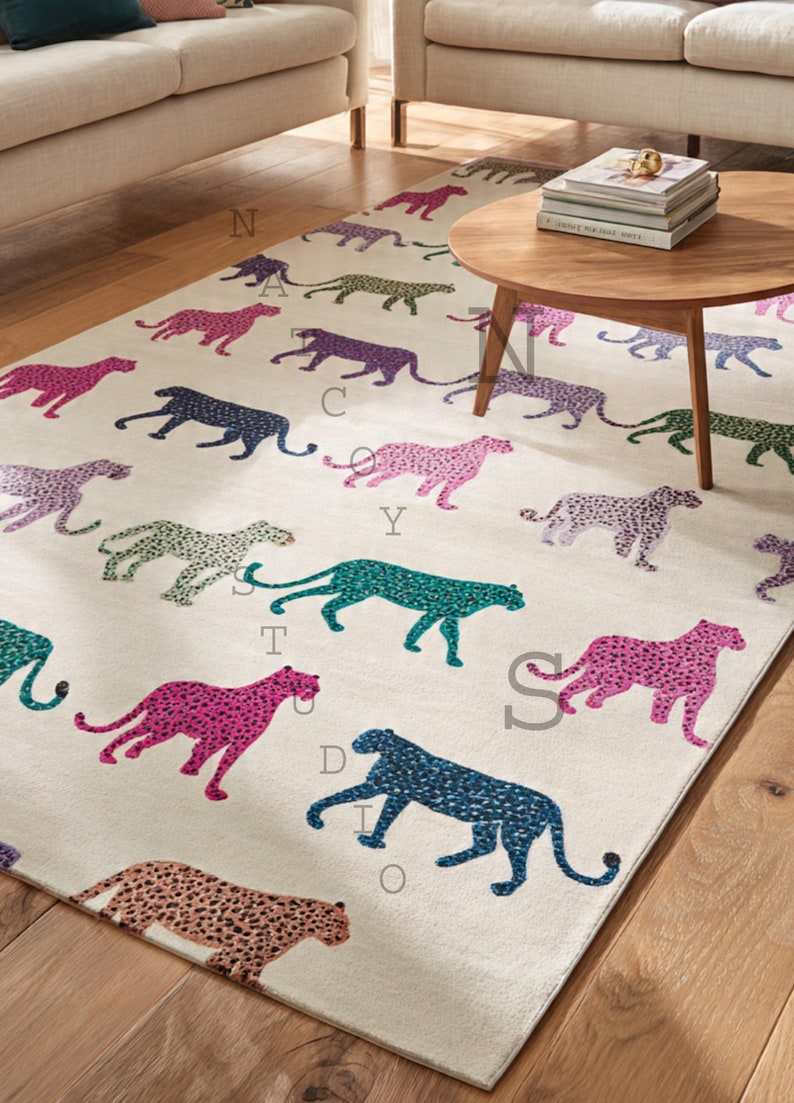 May include: Cream-colored area rug featuring a repeating pattern of stylized cheetahs in various colors, including pink, teal, and navy. The rug is placed on a hardwood floor, with a wooden coffee table and sofa in the background.