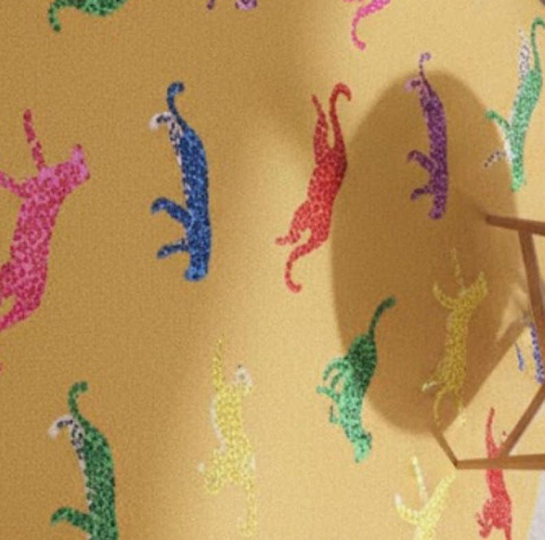 May include: Mustard-colored fabric with a repeating pattern of colorful cheetah silhouettes. The cheetahs are in shades of pink, blue, red, green, yellow, and purple. The fabric has a textured appearance.