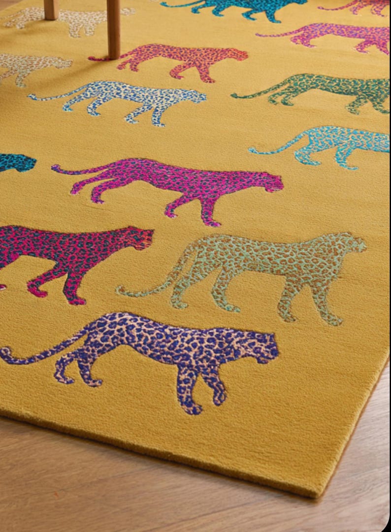 Puede incluir: Alfombra de color amarillo mostaza con un patr&oacute;n repetido de leopardos estilizados en varios colores, incluyendo rosa, azul y verde. El dise&ntilde;o de estampado de leopardo a&ntilde;ade un toque l&uacute;dico y moderno. La alfombra es un elemento decorativo para el hogar.