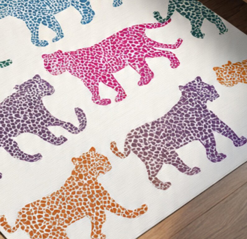 May include: A white rug featuring a repeating pattern of stylized leopard silhouettes in various colors. The leopards are in shades of pink, purple, orange, teal, and green, with a spotted design. The rug is placed on a wooden floor.