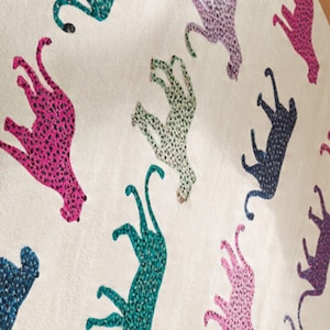 May include: A cream-colored textile featuring a repeating pattern of stylized cheetahs in various colors, including pink, teal, purple, and navy. The cheetahs are covered in small, contrasting spots.