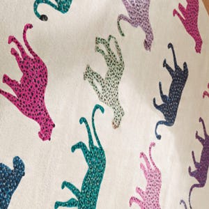 May include: A cream-colored textile featuring a repeating pattern of stylized cheetahs in various colors, including pink, teal, purple, and navy. The cheetahs are covered in small, contrasting spots.