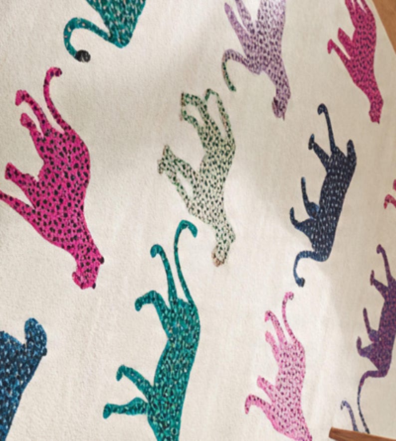 May include: A cream-colored textile featuring a repeating pattern of stylized cheetahs in various colors, including pink, teal, purple, and navy. The cheetahs are covered in small, contrasting spots.