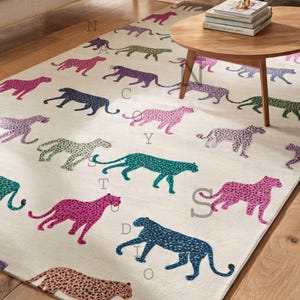 May include: Cream-colored area rug featuring a repeating pattern of stylized cheetahs in various colors, including pink, teal, and navy. The rug is placed on a hardwood floor, with a wooden coffee table and sofa in the background.