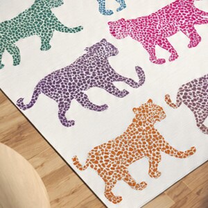 May include: A white rug featuring a repeating pattern of stylized leopard figures in various colors, including green, purple, pink, and orange. The leopard shapes are filled with small, contrasting dots.