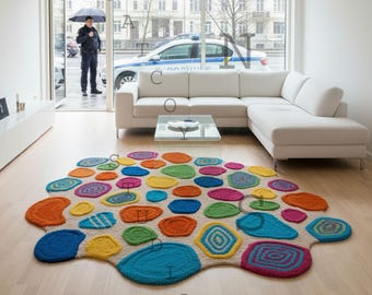 Puede incluir: Una colorida alfombra abstracta con un fondo beige y varias formas circulares multicolores. La alfombra presenta tonos de azul, verde, naranja, amarillo y rosa. La alfombra está colocada sobre un suelo de madera clara en un salón moderno.