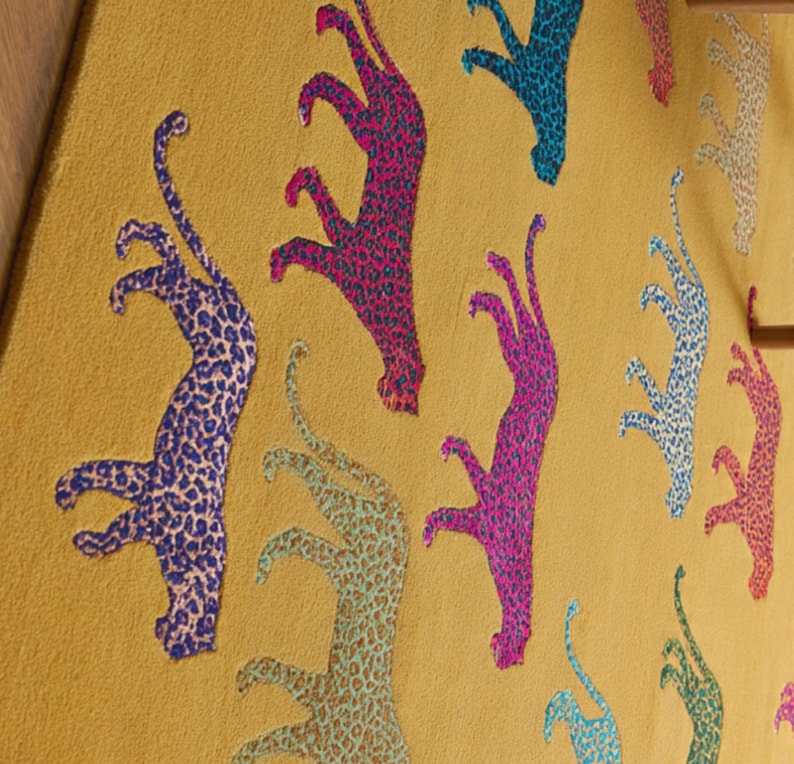 Puede incluir: Tela de color mostaza con un patr&oacute;n repetido de figuras de leopardo estilizadas en varios colores. Los leopardos son de colores vibrantes, incluyendo azul, rosa y verde, con un dise&ntilde;o moteado. Un textil din&aacute;mico y original.