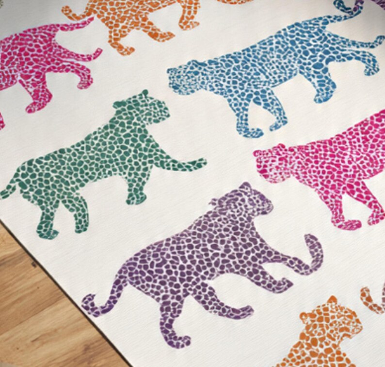 May include: A white textile featuring a repeating pattern of stylized leopard silhouettes in various colors. The leopards are depicted in shades of pink, orange, blue, green, and purple, with a speckled design. The overall aesthetic is playful and vibrant.