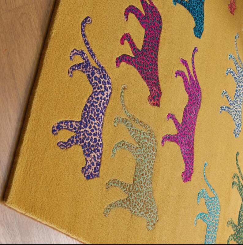 Puede incluir: Alfombra de color amarillo mostaza con un patr&oacute;n repetido de figuras de leopardo estilizadas en azul, rosa y turquesa. Las figuras de leopardo tienen un dise&ntilde;o moteado.
