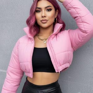 May include: A cropped, pale pink puffer jacket with a high collar and a front zip. The jacket is worn over a black top and paired with black leather trousers. A gold necklace and hoop earrings complete the outfit.